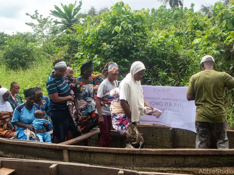 A boat at the riverbank, women aboard and a volunteer holding the banner.