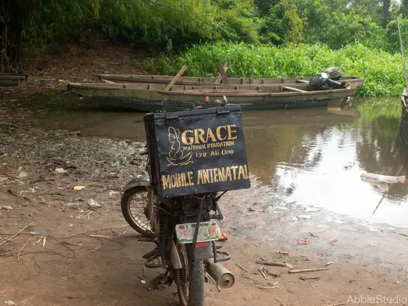A motorcycle at the water's edge carrying a lettered box that reads Grace Maternal Foundation, Mobile Antenatal.