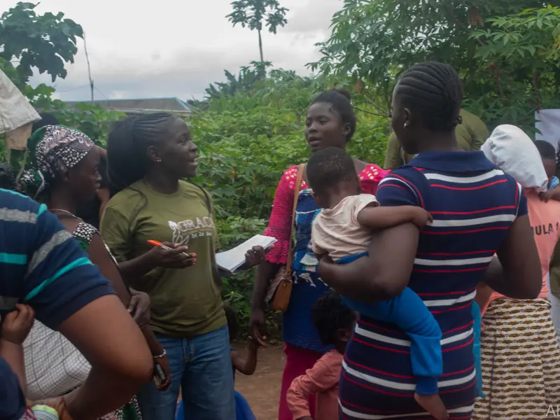 Volunteers in Foundation T-shirts talking with mothers carrying infants.