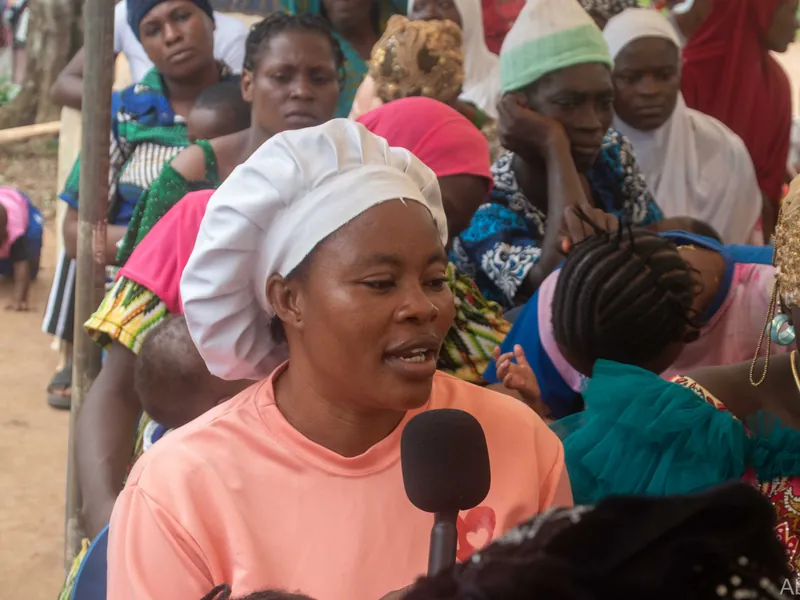 A woman speaking into a microphone among seated attendees.