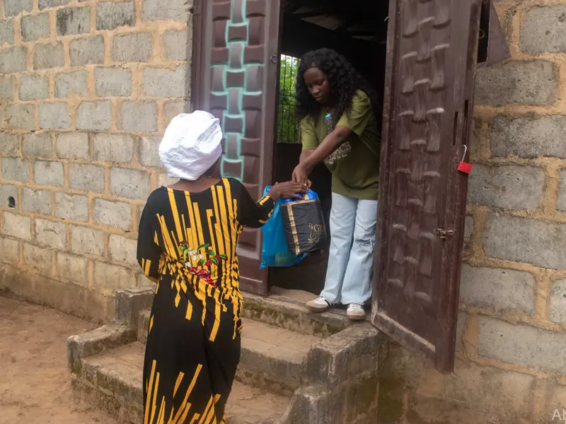 A volunteer at a doorway handing a bag to a woman.