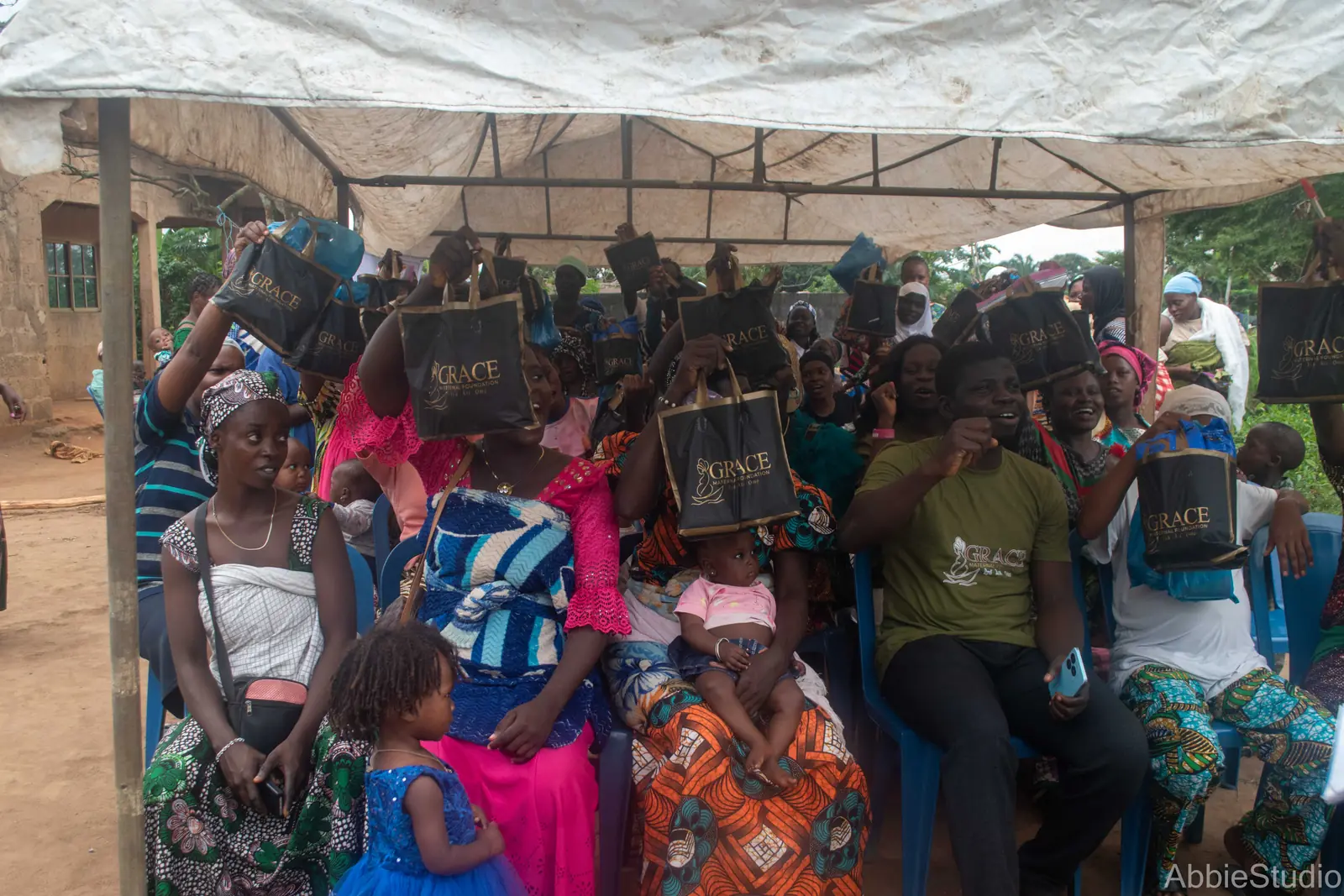 Women seated under the outreach tent in Ikogbo, holding up the gift packs they received.