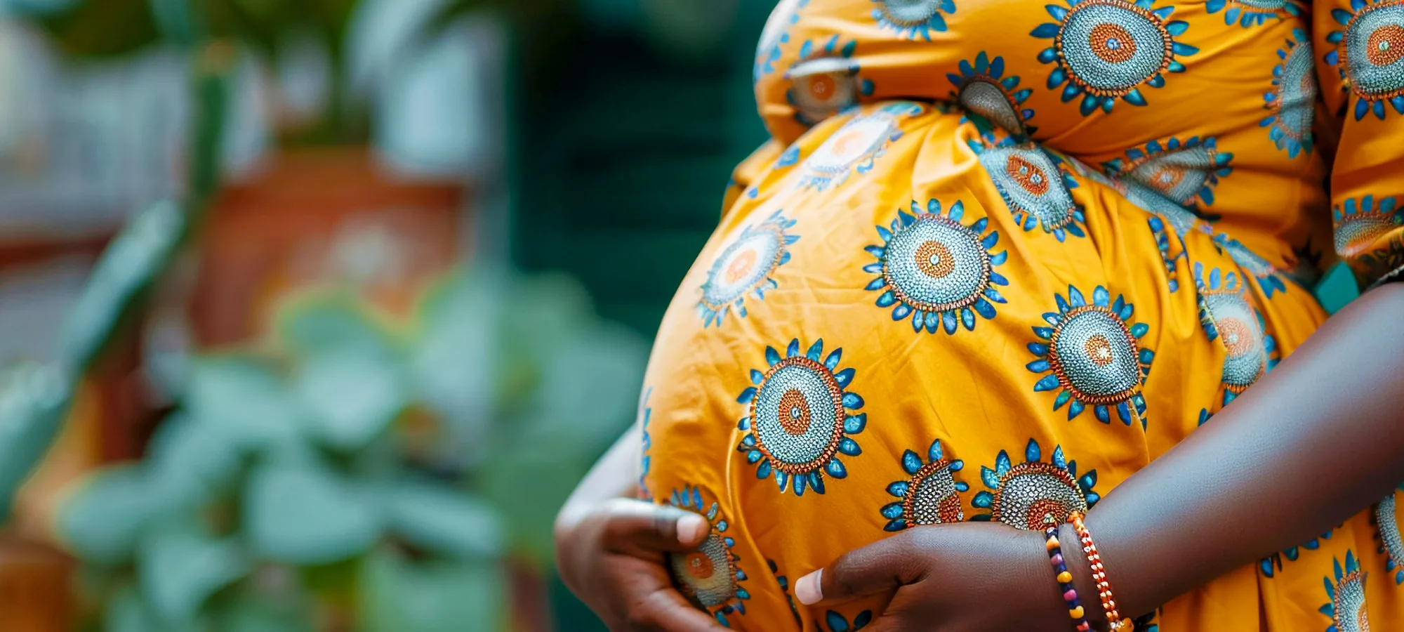 A pregnant woman in Ankara cloth, both hands resting on her body.