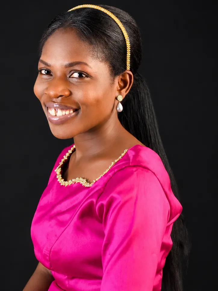 A studio portrait of a seated woman in a pink dress, smiling towards the camera.