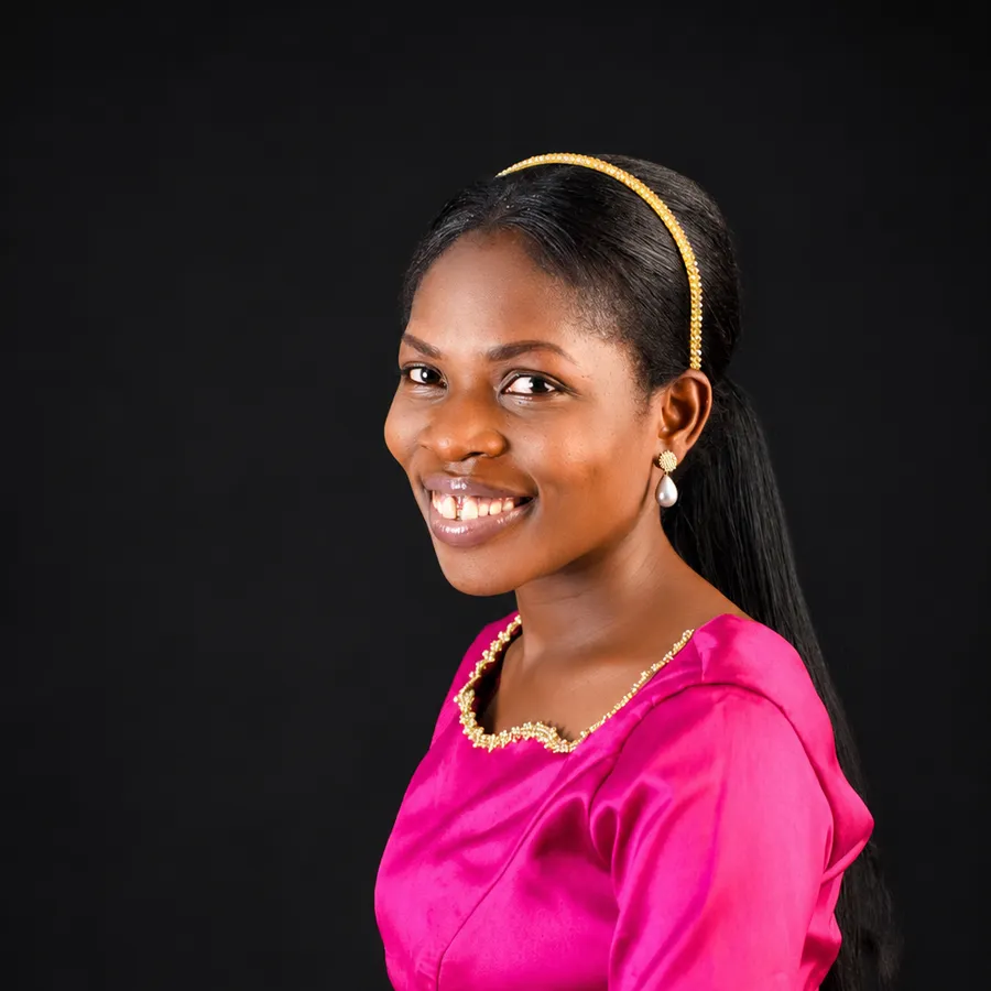 A studio portrait of a seated woman in a pink dress, smiling towards the camera.
